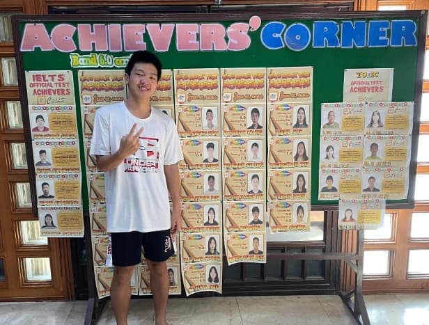 CPILS 교내 Achievers' Corner 게시판 앞에서 브이 포즈를 하는 Anderson Tsai. 게시판에는 IELTS와 TOEIC 목표 달성자가 게시되어 있다